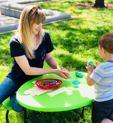 A childcare worker plays with a boy at a small table