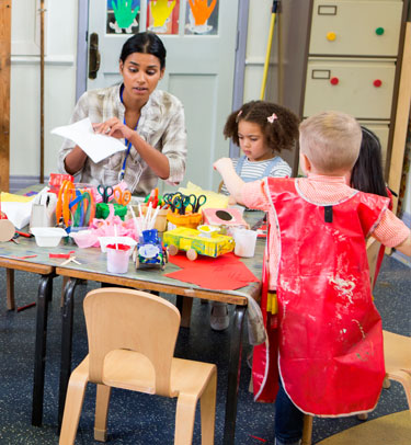 A caregiver is doing an art project with two young children.