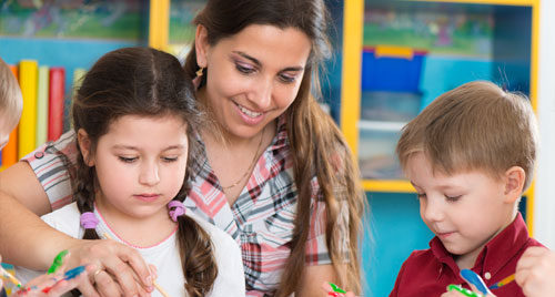 A childcare provider teaches three young children to paint.