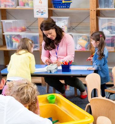 A young woman is working on a craft project with two small children.