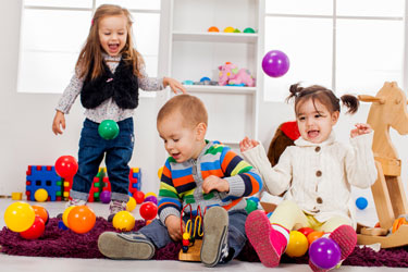 Three young children play with colored balls while sitting on the floor.