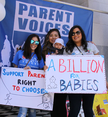 A group of parents hold signs voicing their concerns at a parent voices rally.